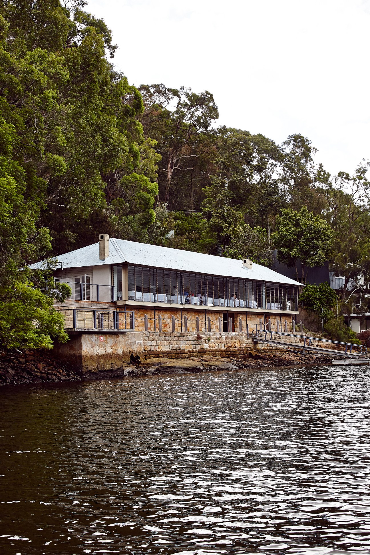 Glenn Murcutt-designed Berowra Waters Inn sits on stilts above the Hawkesbury River, surrounded by dense bushland.