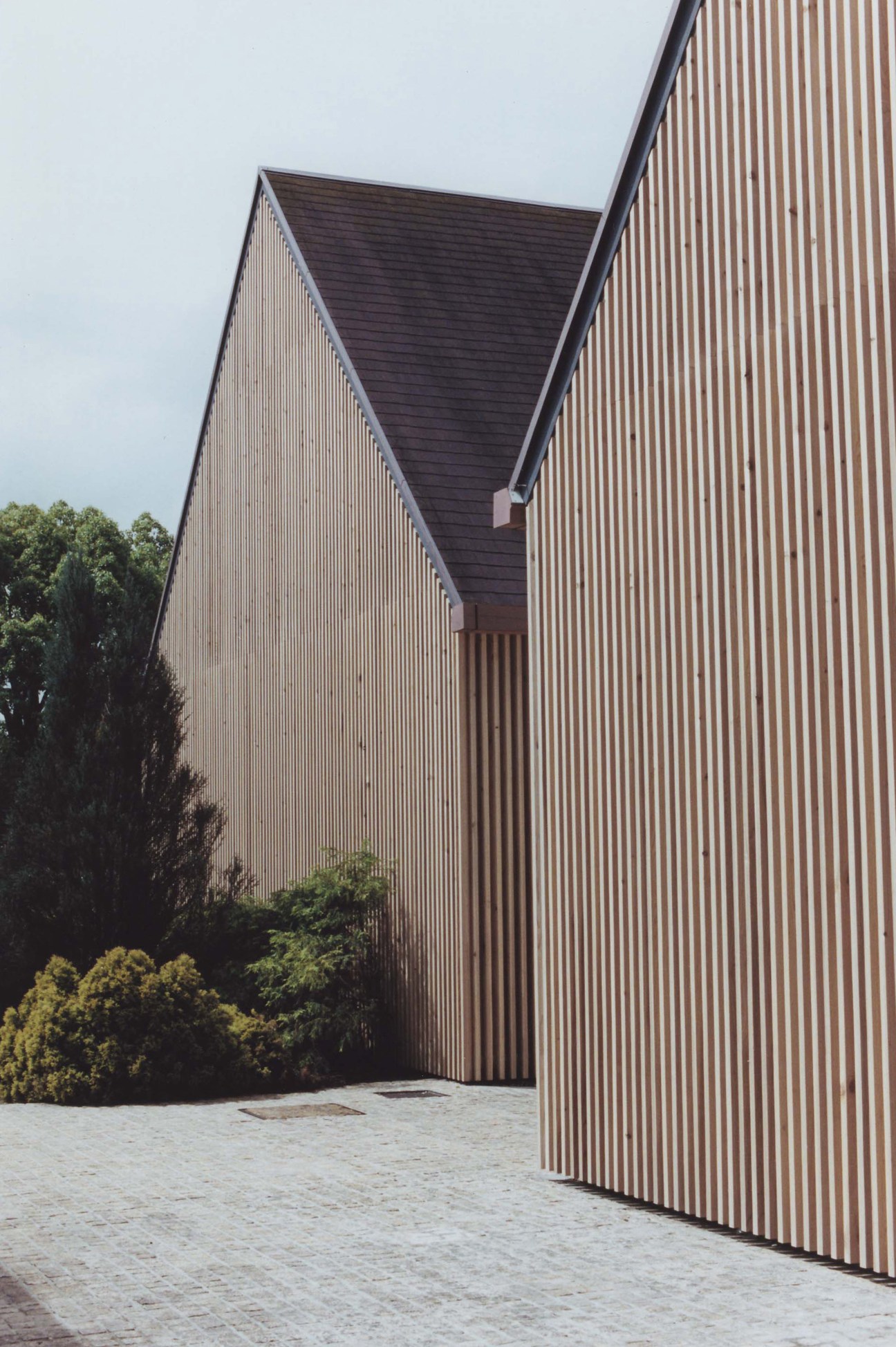 Modern angular building with corrugated metal siding and geometric forms surrounded by landscaping.