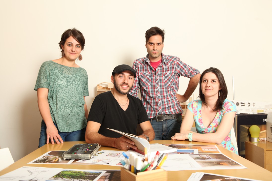 Four architects posing at a wooden table with design materials and sketches in a studio.