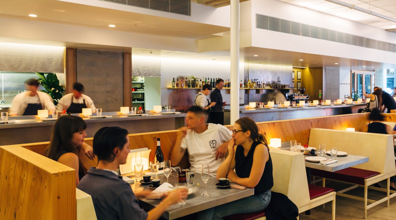 Interior of Supernormal restaurant in Melbourne with diners at tables and chefs working at an open kitchen counter.
