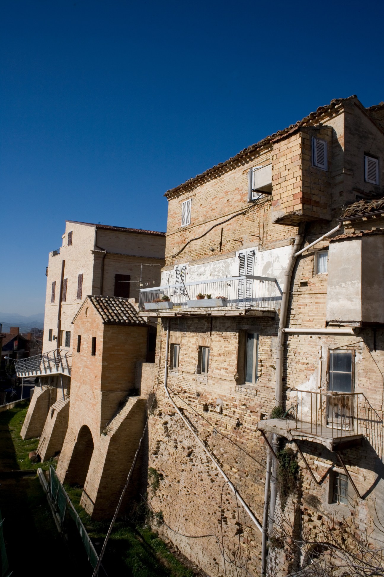 Medieval hilltop town with terracotta-roofed stone buildings against clear blue sky in Montegranaro, Italy.