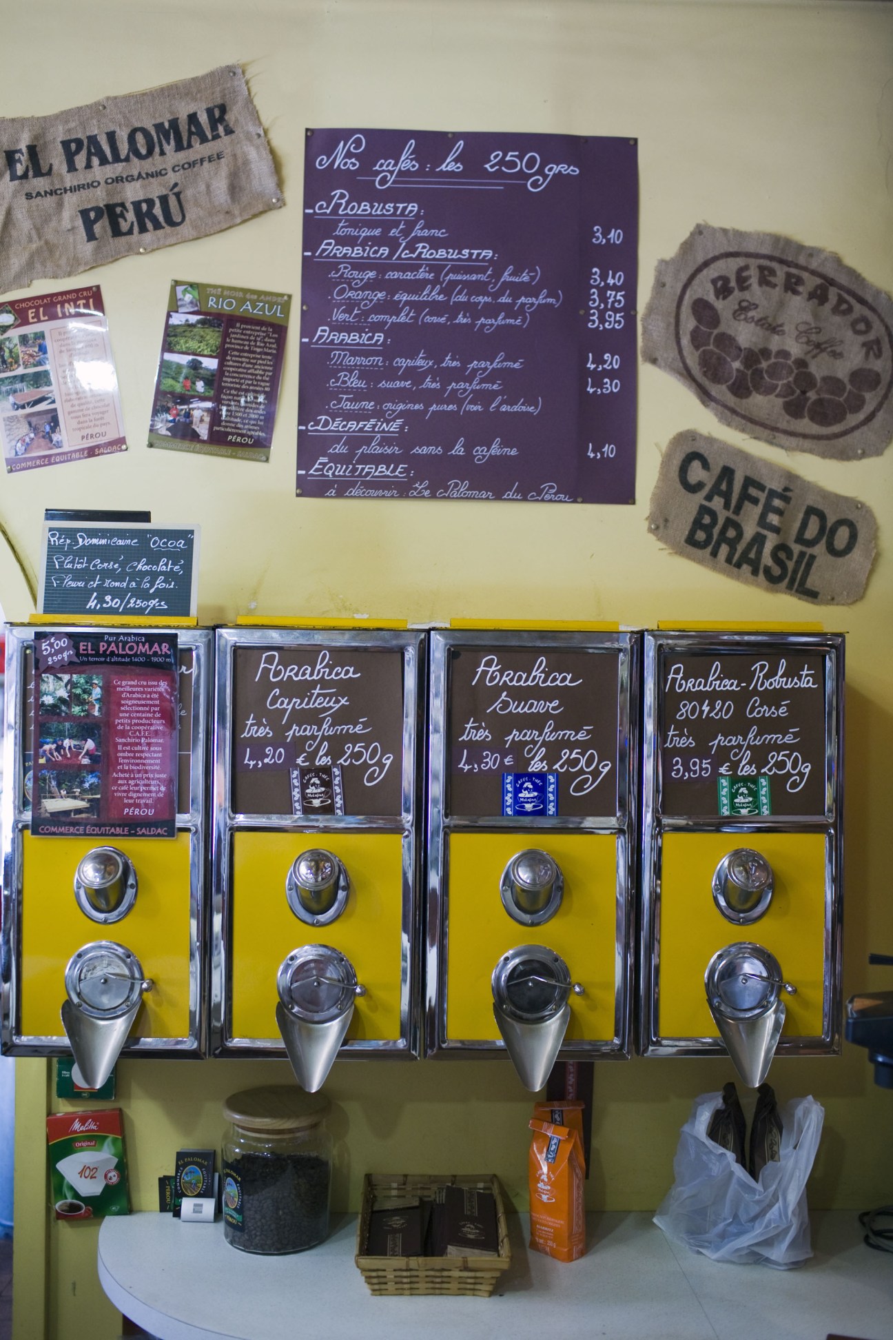 Café Moka Fina's yellow coffee dispensers with hand-written menus and coffee bean sacks displayed on pale yellow wall.