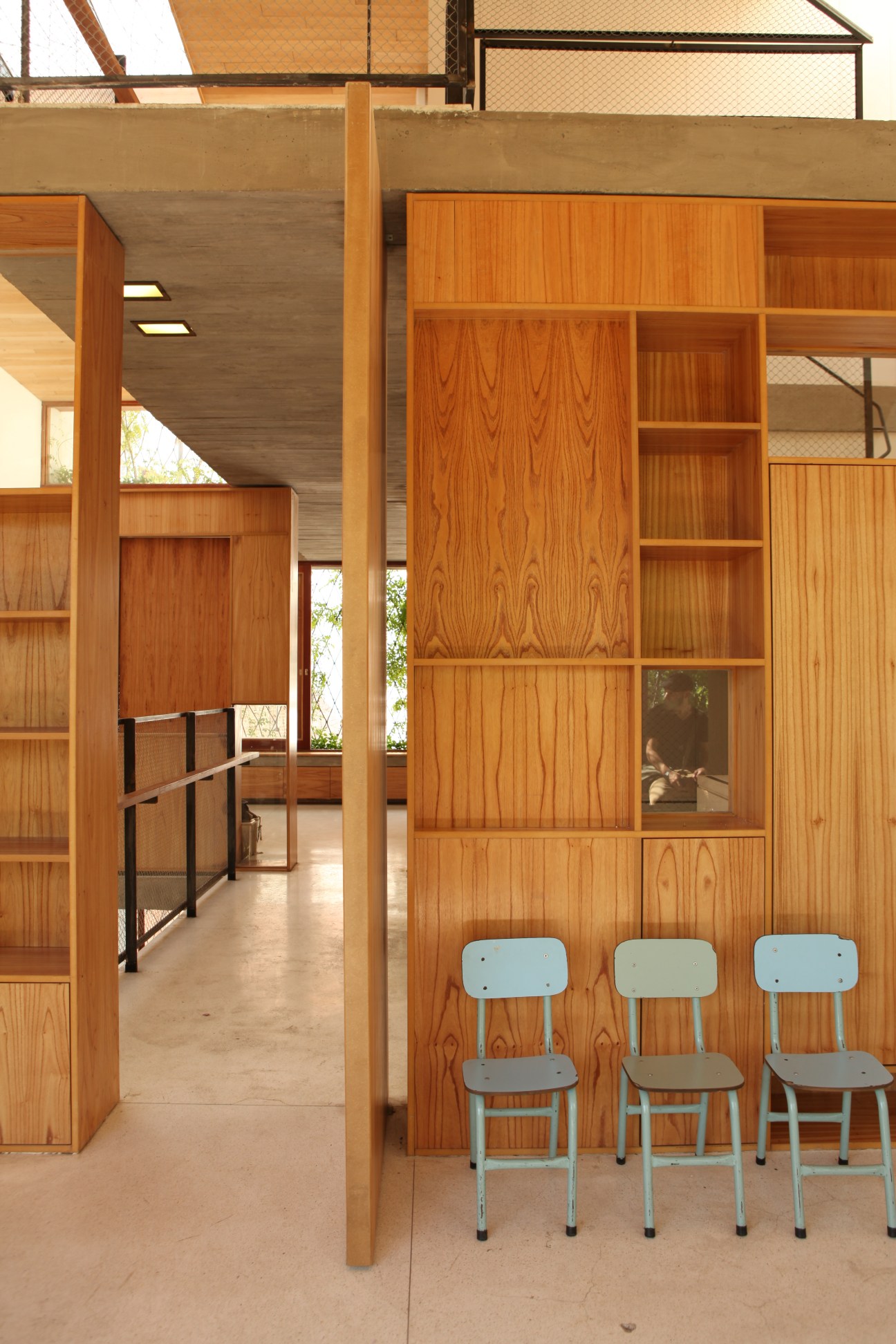 Interior space with chinaberry wood panelling walls, shelving, and three light blue chairs against wooden cabinetry.
