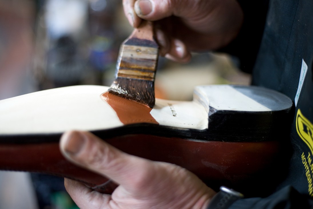Craftsman Bruno Falappa applies paint to a brown leather shoe sole with a brush.