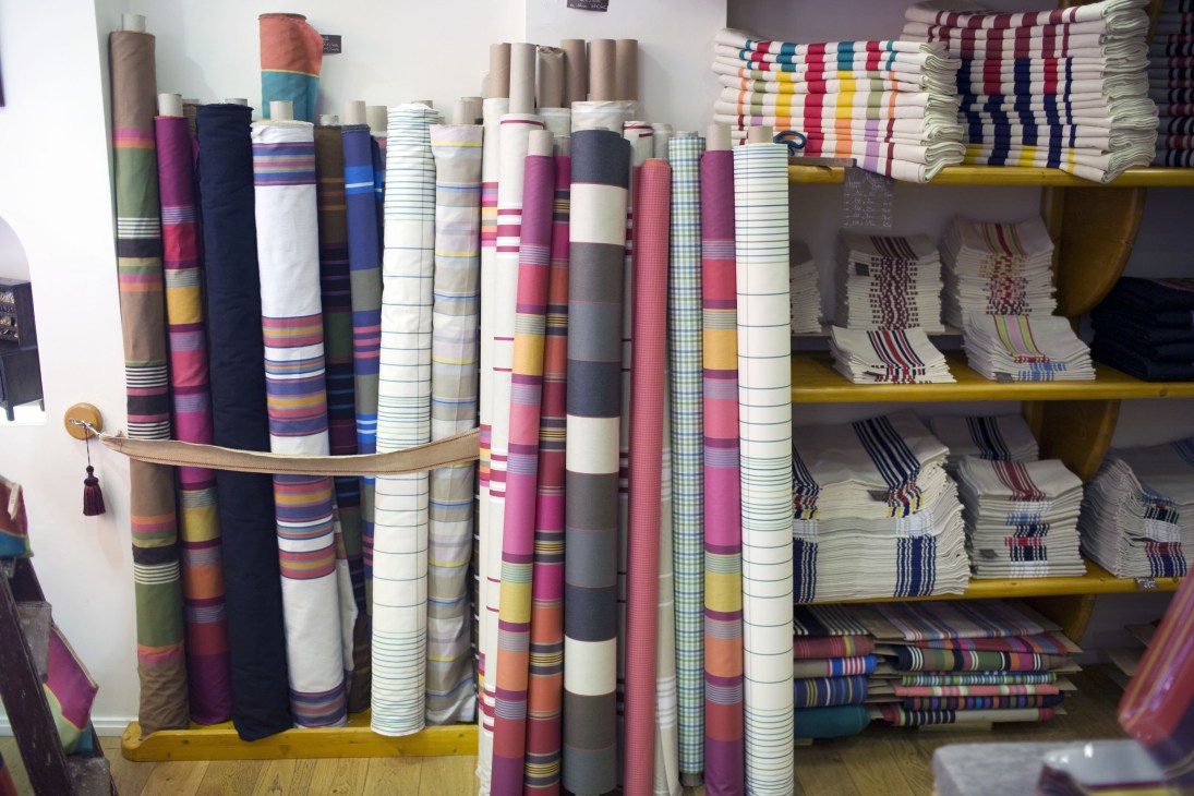 Colorful rolled Basque linen textiles with striped patterns displayed in a shop window.