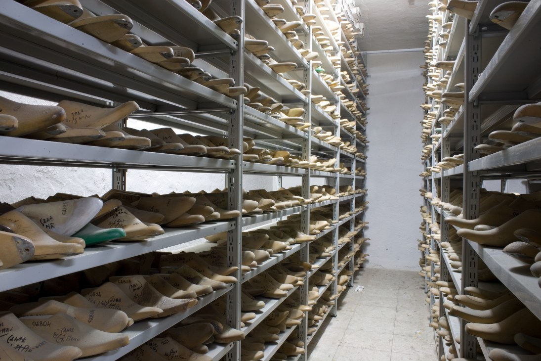 Metal shelving racks filled with wooden shoe lasts at Formificio Veregra, each labeled with handwritten measurements and customer details.