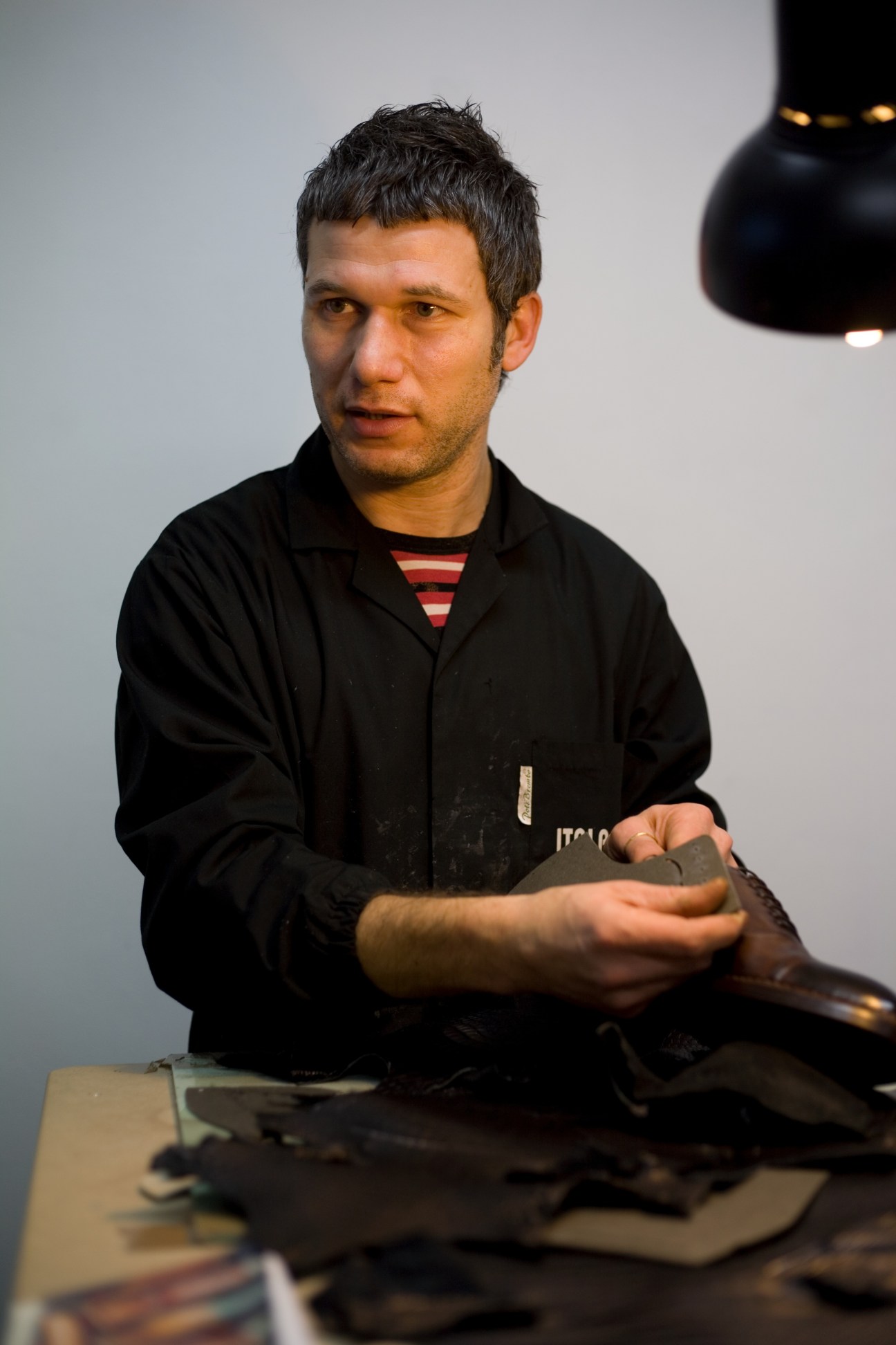 Man in black jacket holding leather shoe material at workbench with samples.