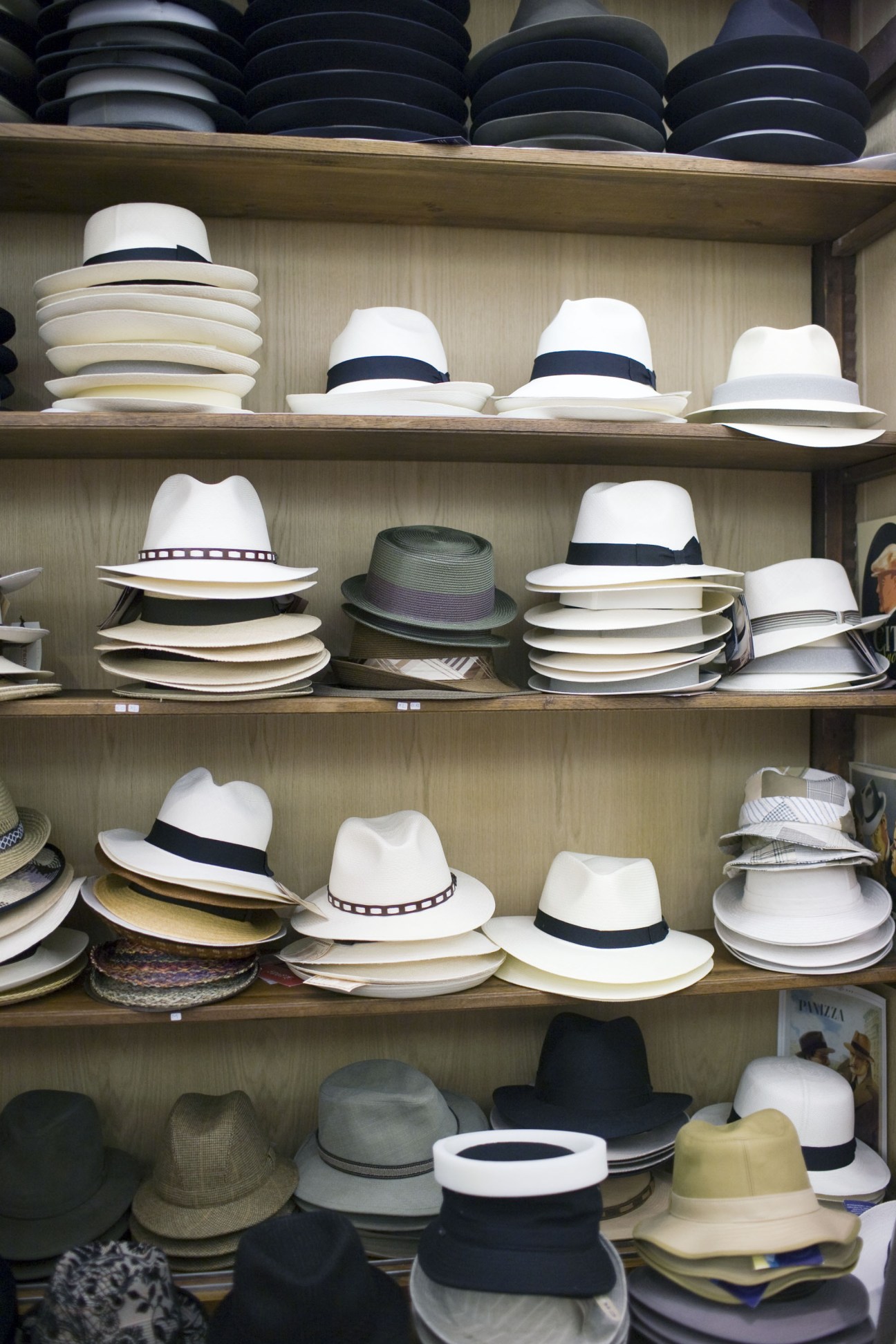 Shelves displaying an array of straw and felt hats in white, black, and natural colors at Divine milliner shop.