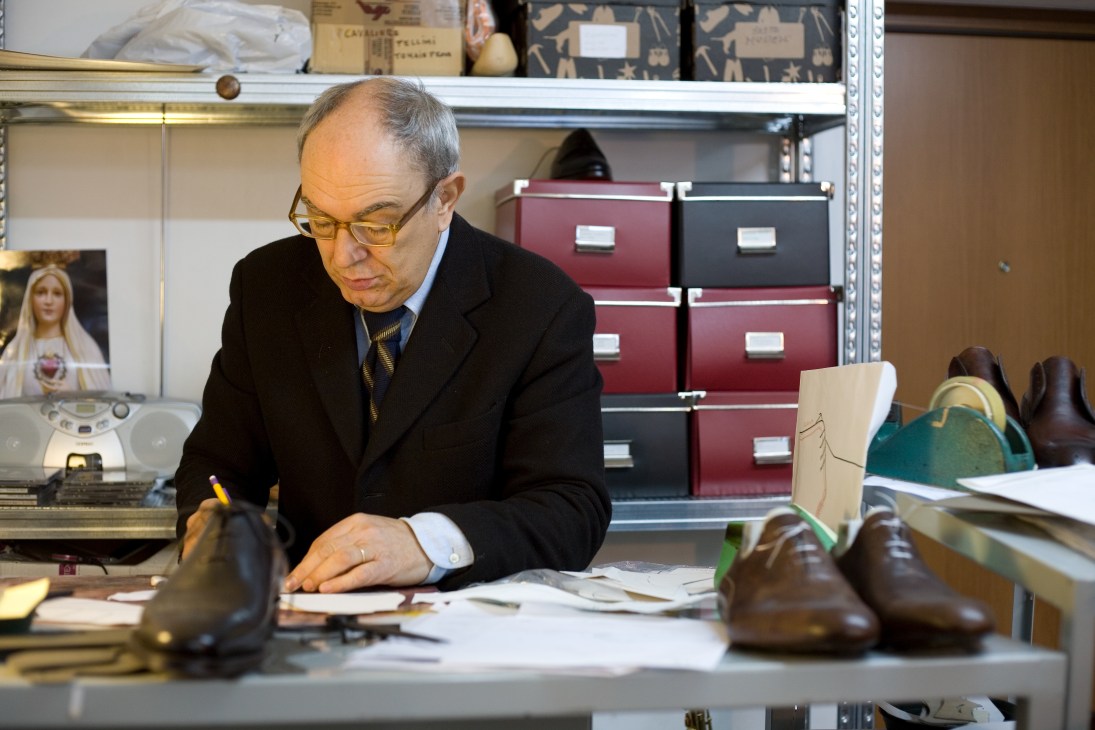Manfredo Gazzani sketches shoe designs at a desk in the Bontoni workshop, surrounded by leather shoes and filing boxes.