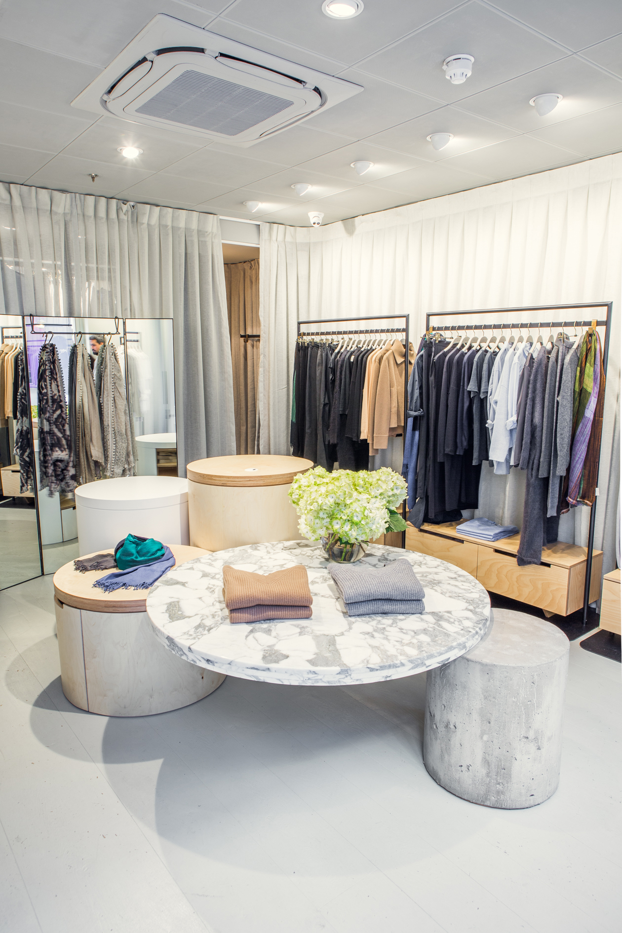 Interior of Jac+Jack store in London showing marble table display with clothing and racks of merchandise.