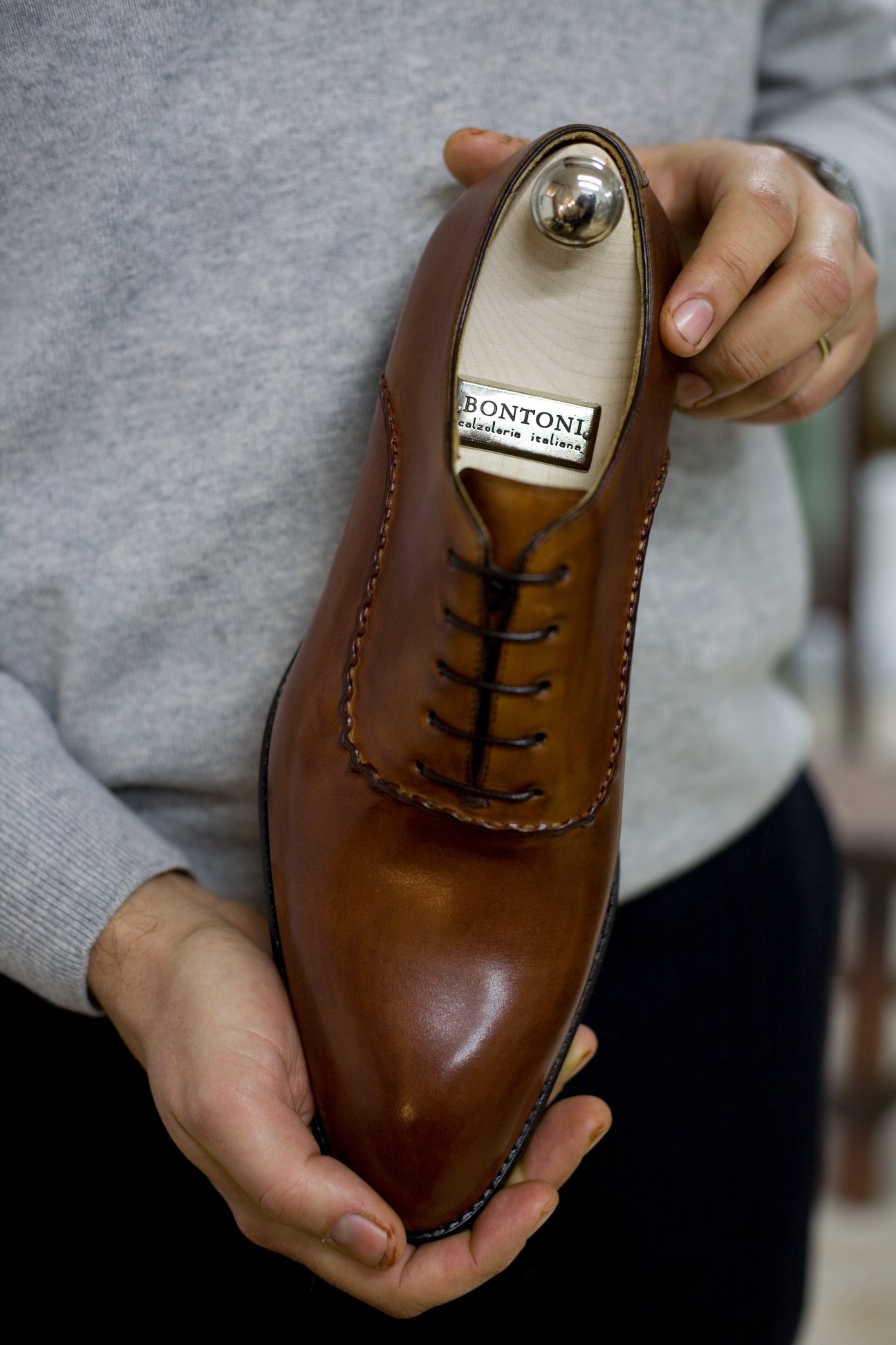 A hand holding a brown leather Bontoni oxford shoe displaying the brand label inside.