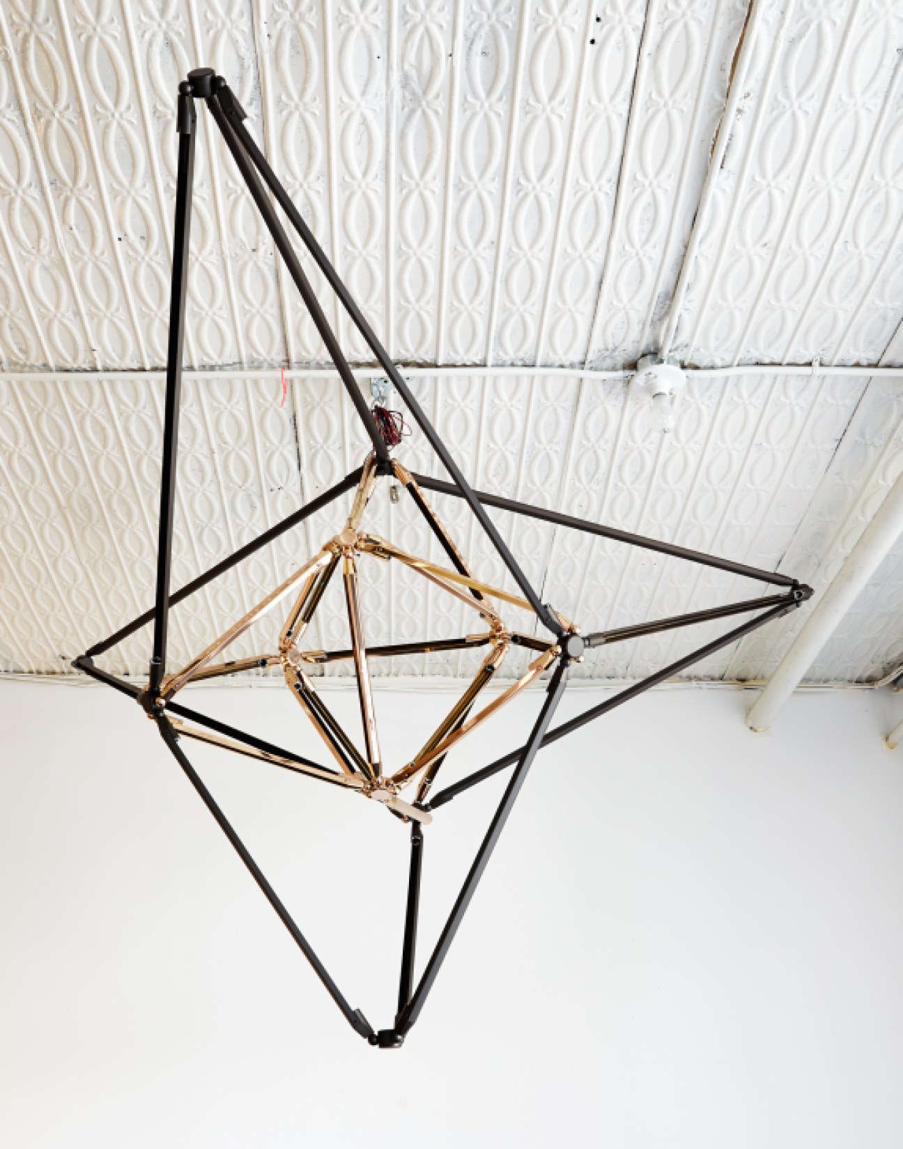 Bec Brittain's Shy series brass chandelier with geometric metal framework in black and gold tones.