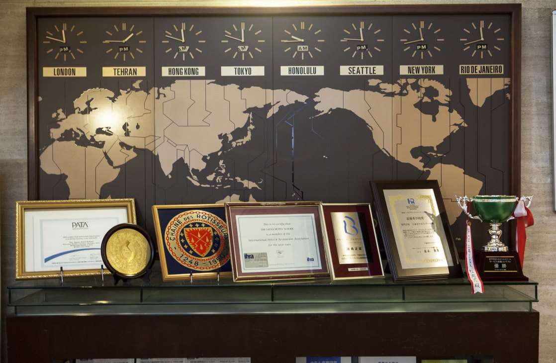 World clock and awards displayed in the Japan Hotel School lobby, showing time zones and certificates.