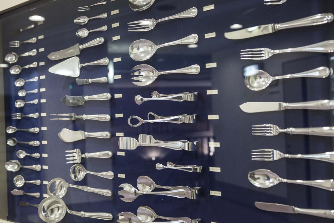 A wall display of silverware and cutlery arrangements showing various utensils organized in rows against a dark background.