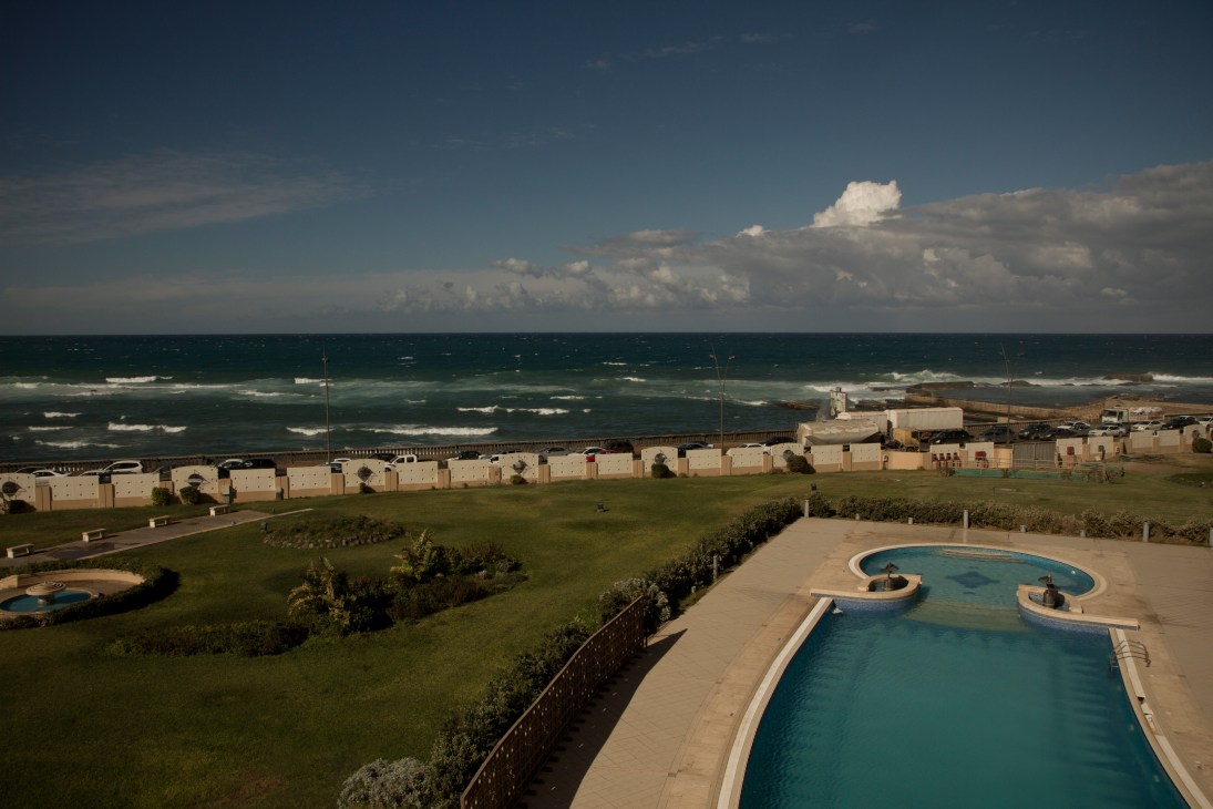 Corinthia Hotel overlooking Libya's Mediterranean coastline with swimming pool in foreground and beachfront compounds beyond.