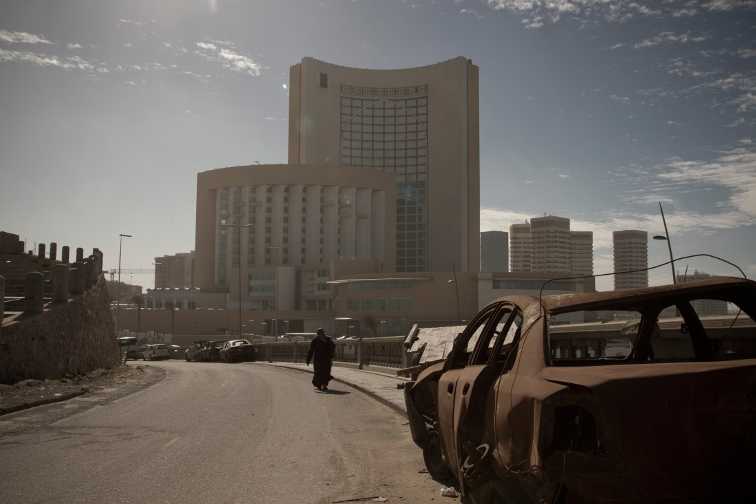 Burnt-out car wreckage in foreground with Corinthia Hotel's distinctive curved towers behind in Tripoli.
