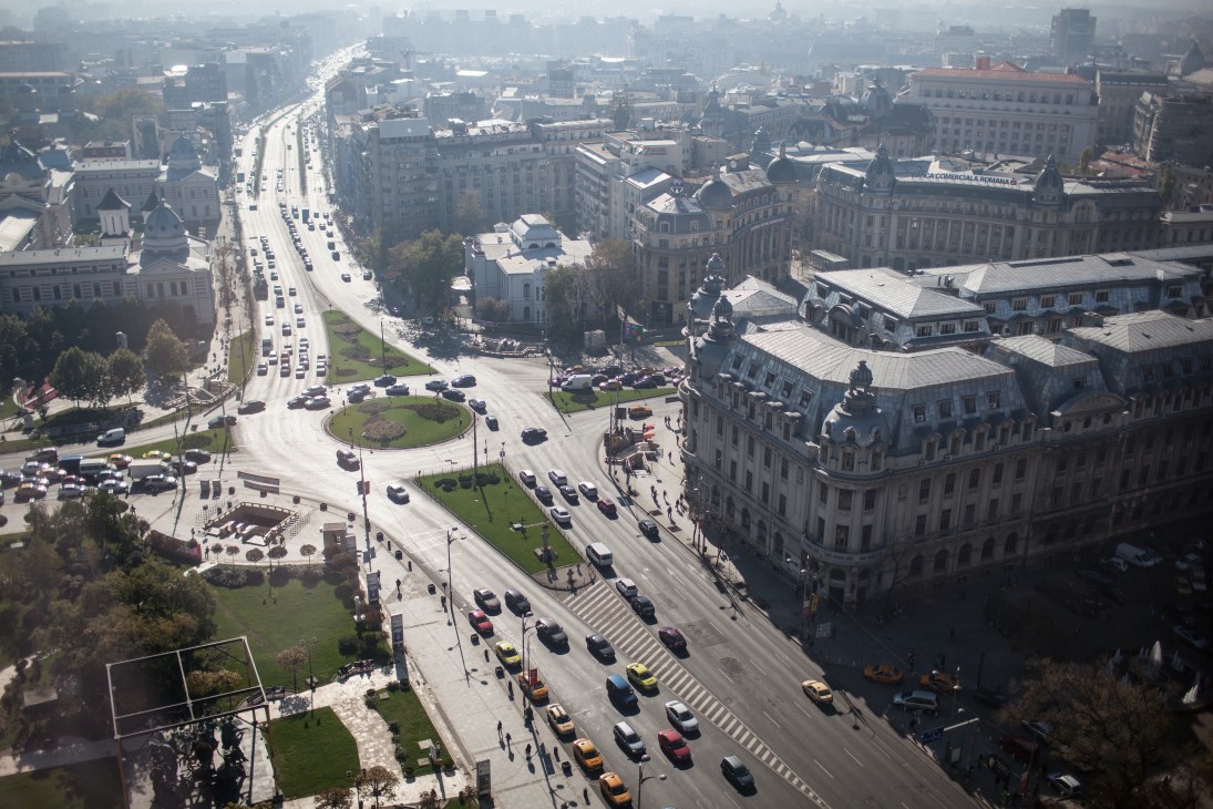Aerial view of Bucharest showing wide boulevards, European architecture, and urban sprawl under hazy sky.