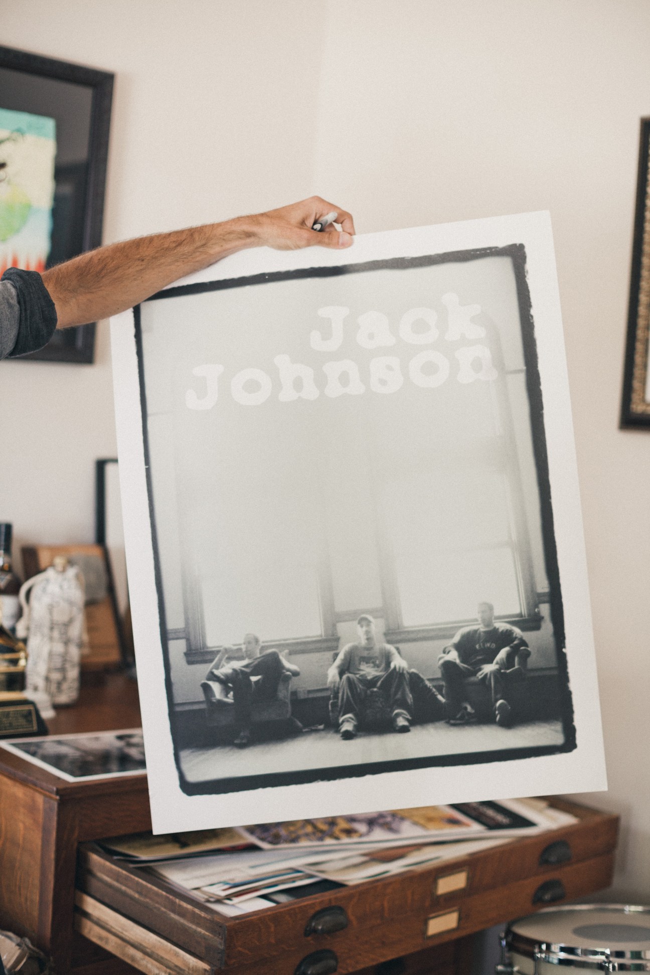 Hand holding an early Jack Johnson poster showing band members sitting against a large window.