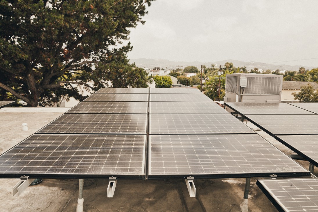 Solar panels installed on a flat rooftop with Los Angeles hillside and palm trees visible in the background.
