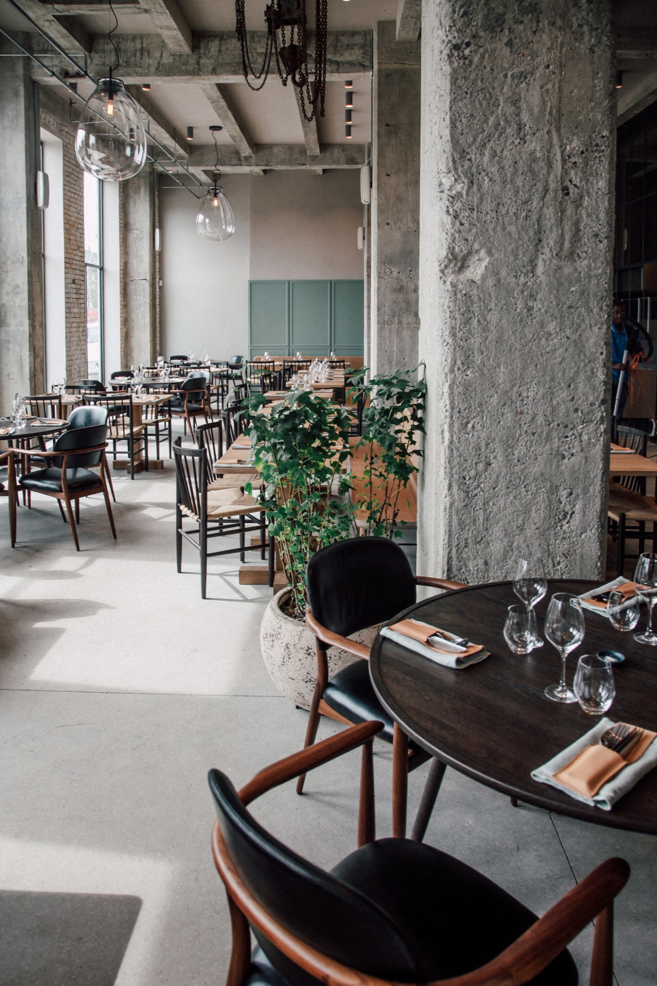 Interior of SpiseBar Nr.20 restaurant in Copenhagen with wooden tables, black chairs, and industrial concrete architecture.