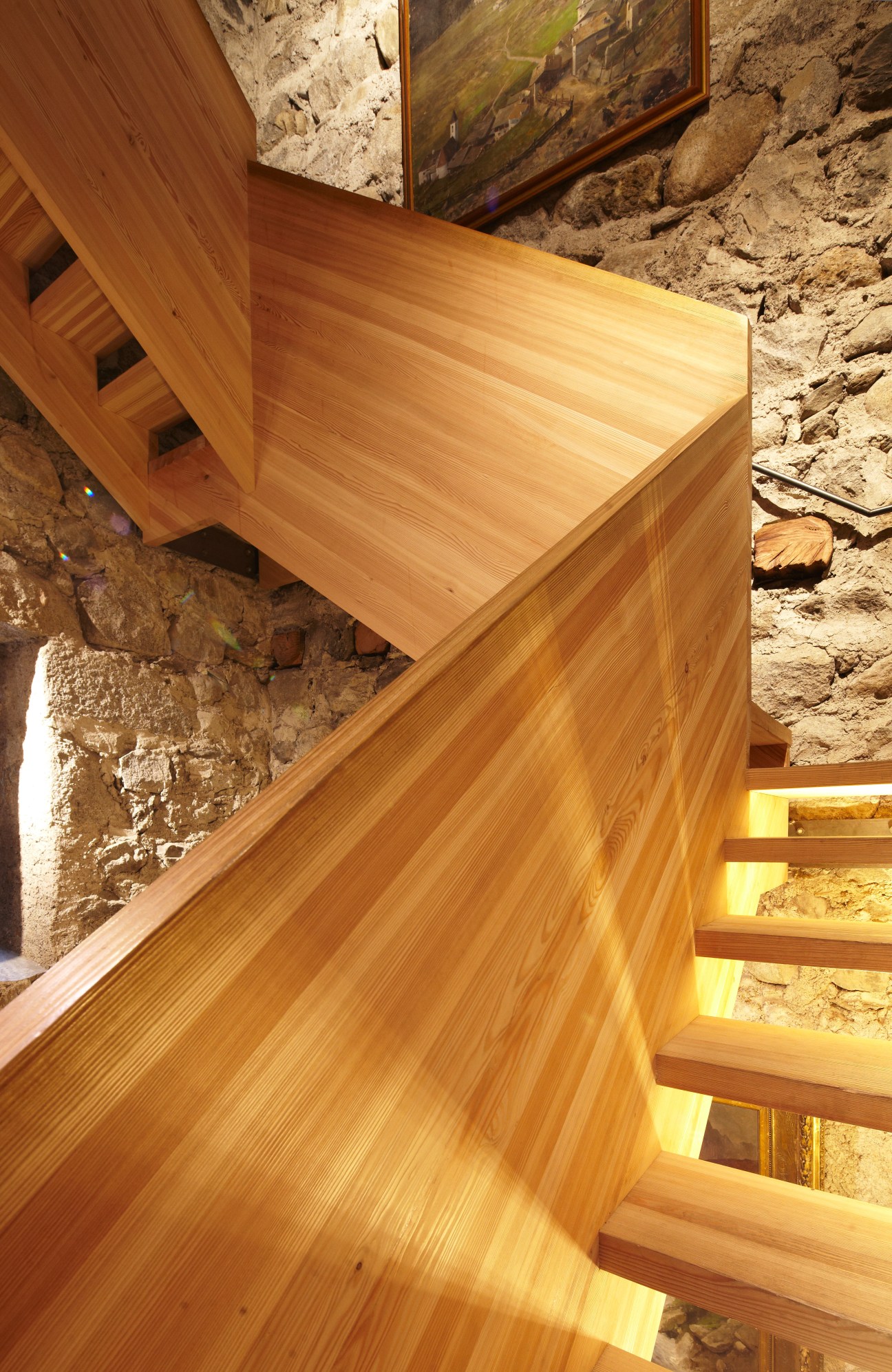 Curved wooden larch staircase with illuminated steps against weathered stone walls in Messner Mountain Museum.