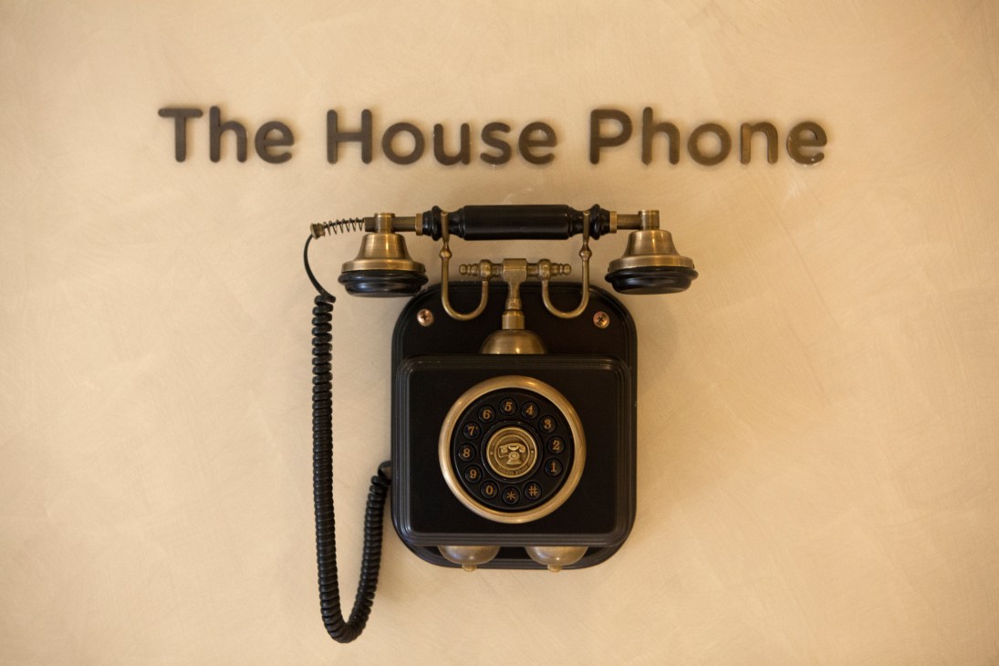 Vintage black and brass rotary telephone mounted on cream wall with 'The House Phone' text above.