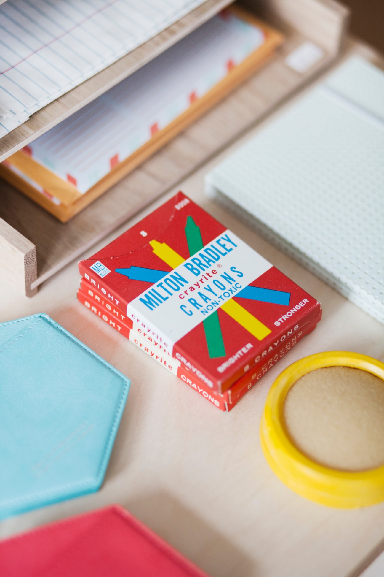 Colorful crayons and office supplies arranged on a light wooden desk surface.