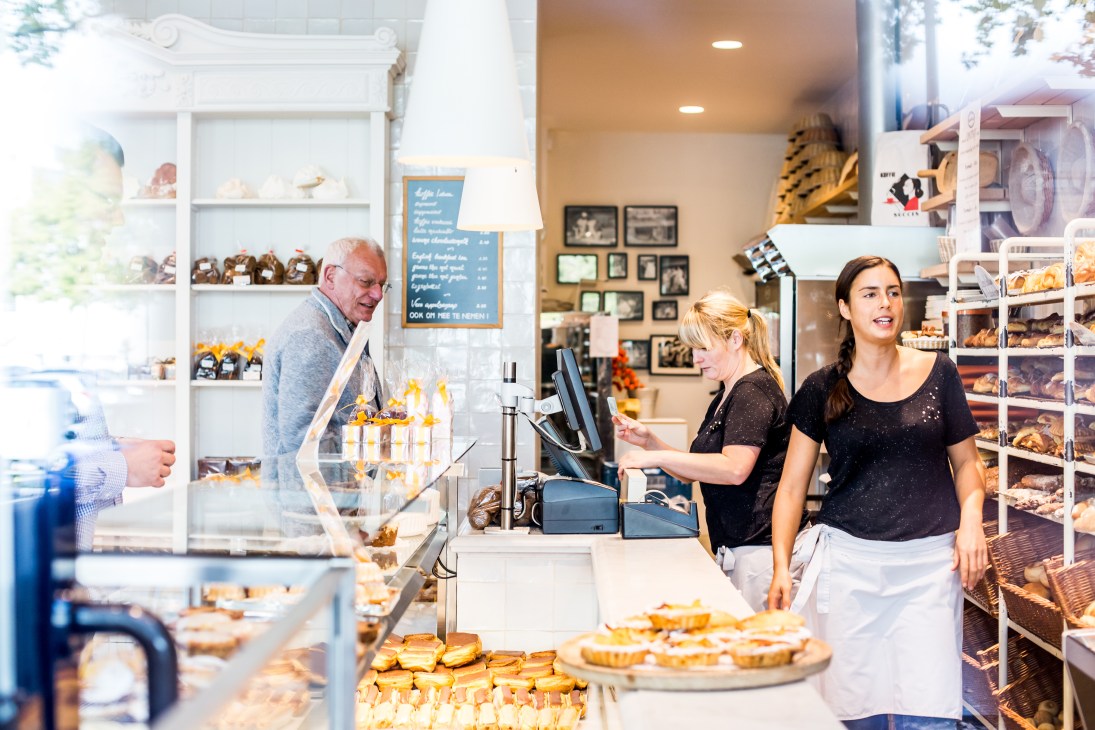Interior of Dellafaille patisserie with staff and pastries displayed in white shelving and counter.
