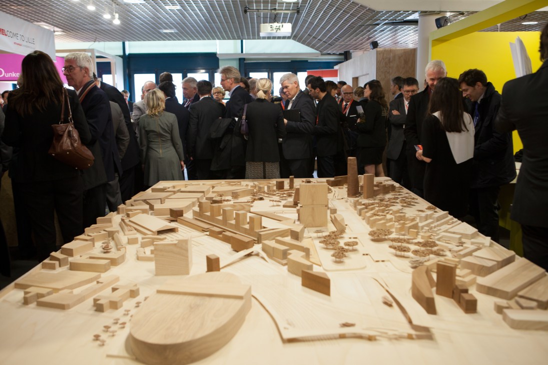 Architects and developers examine a wooden architectural model at Mipim property fair.