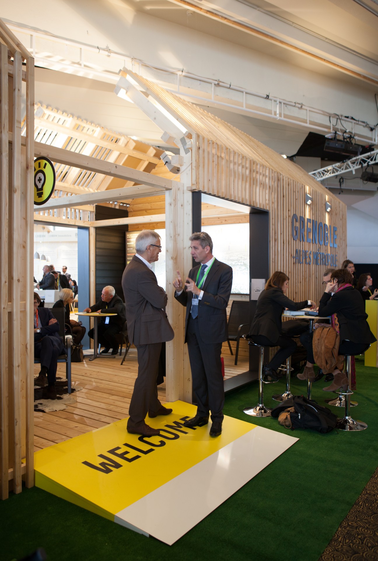 Two businessmen converse at Grenoble's wooden exhibition stand with sustainable design features at Mipim.