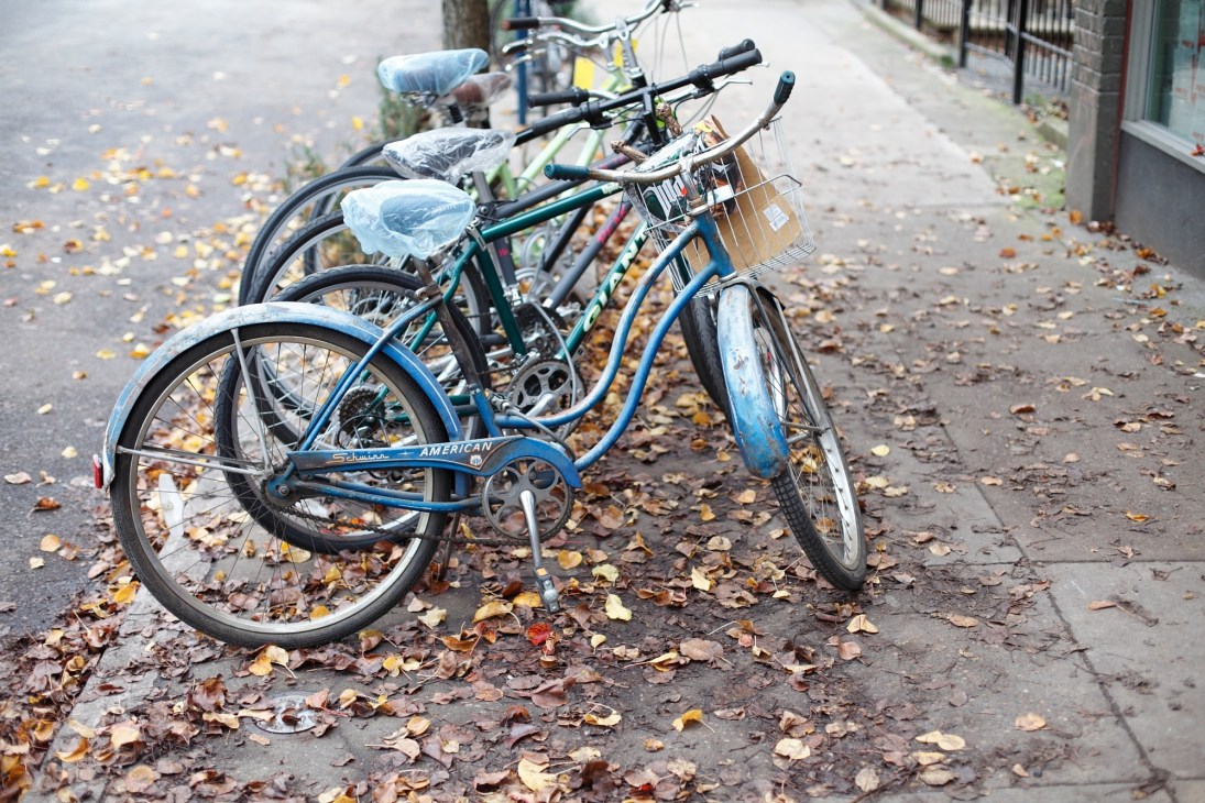 Three bicycles with baskets parked on a sidewalk covered with autumn leaves.