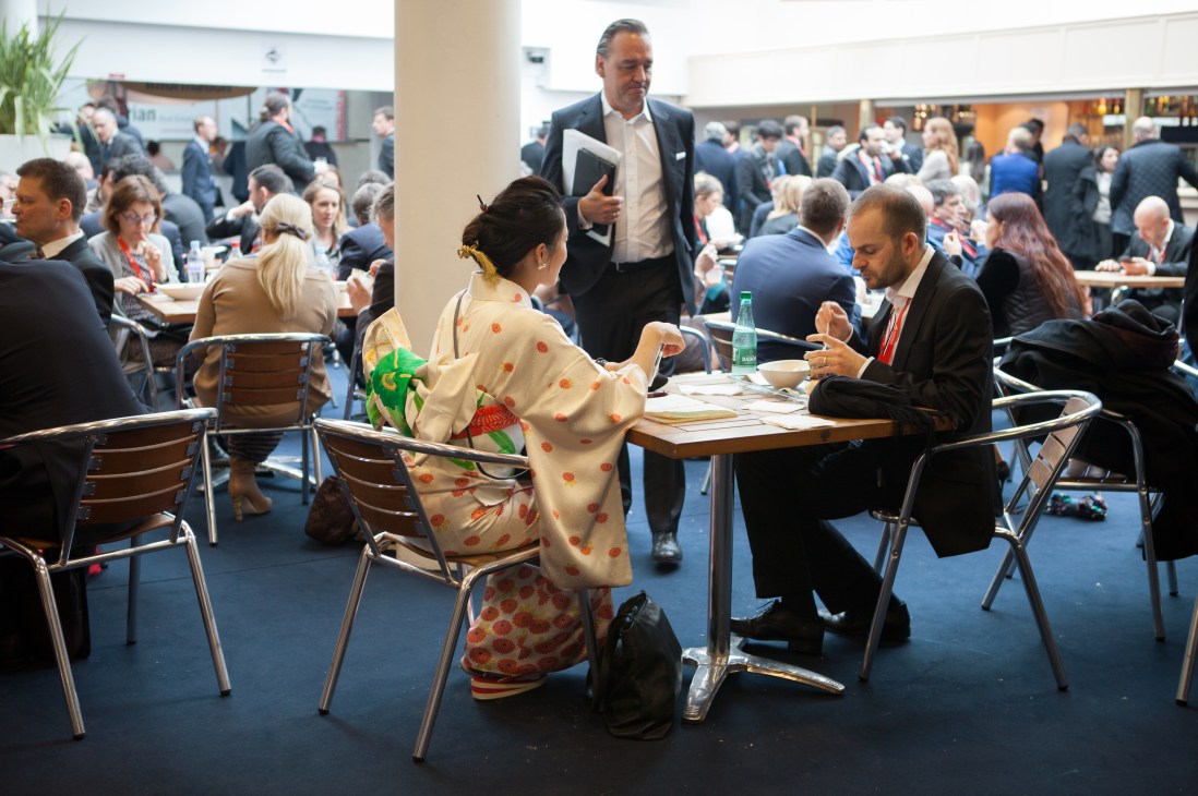Business professionals from diverse backgrounds meet and converse at tables during Mipim property fair.