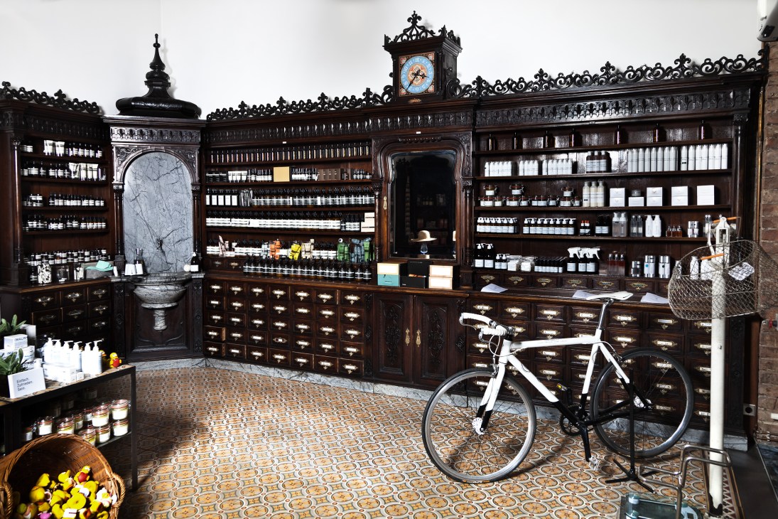 Interior of Saint Charles Apothecary in Vienna with ornate dark wood cabinetry, shelves of products, a white bicycle, and decorative clock.