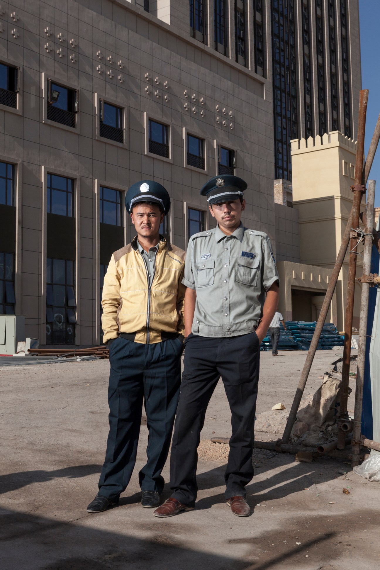Two security guards in uniforms standing outside a modern concrete construction site in Kashgar.