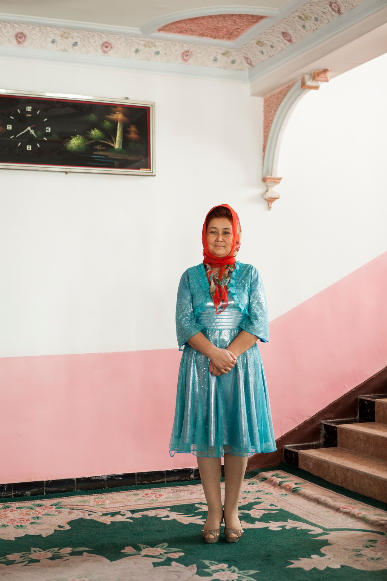 Zytunam Turdi, Seman Hotel employee, stands in a hallway wearing a turquoise dress and red headscarf.