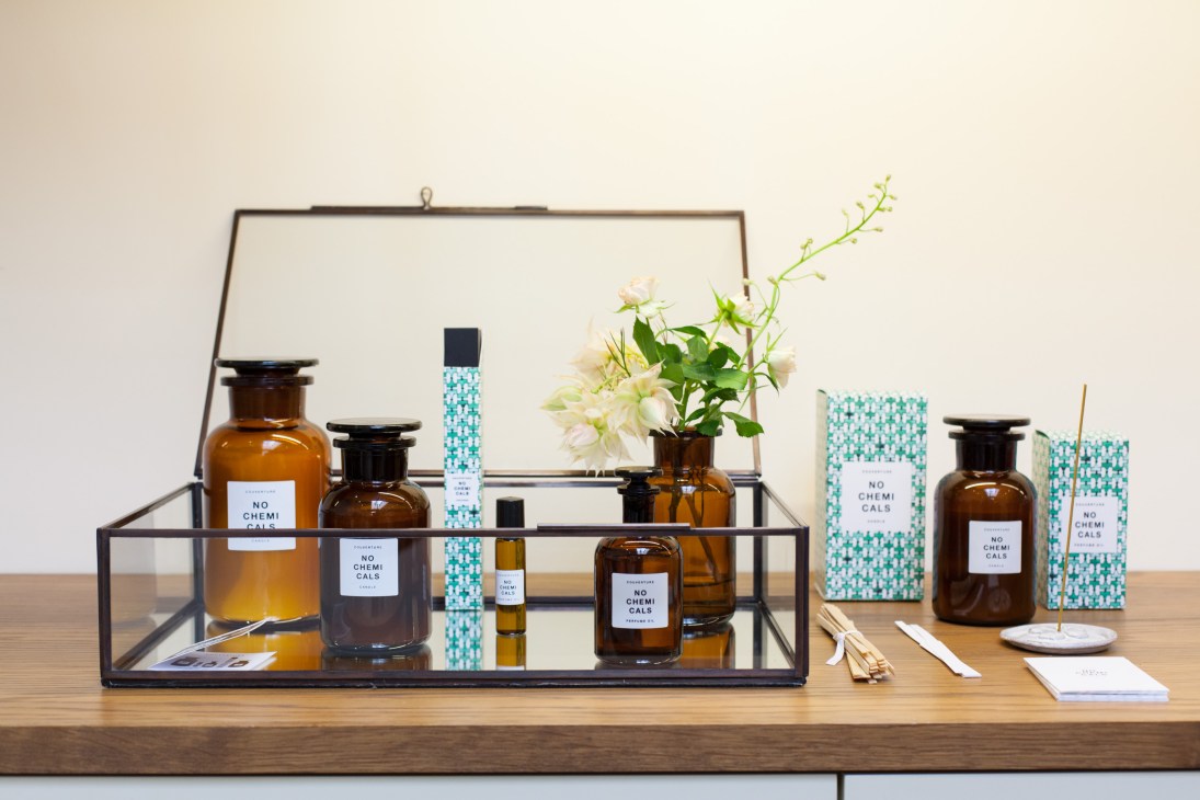 Display of No Chemicals branded amber glass bottles and turquoise patterned boxes arranged in a glass case with fresh flowers.