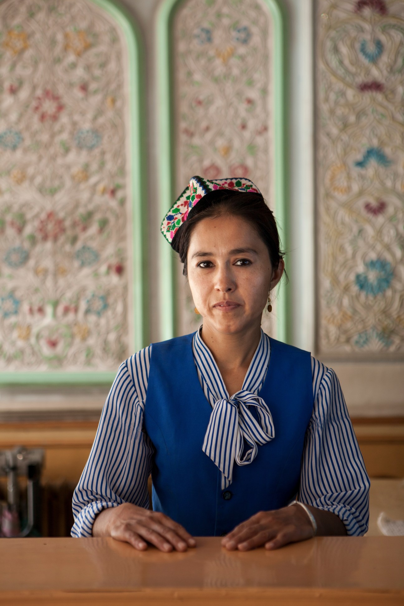 Floor manager at the Seman Hotel in Kashgar wearing traditional Uyghur headwear and blue vest.
