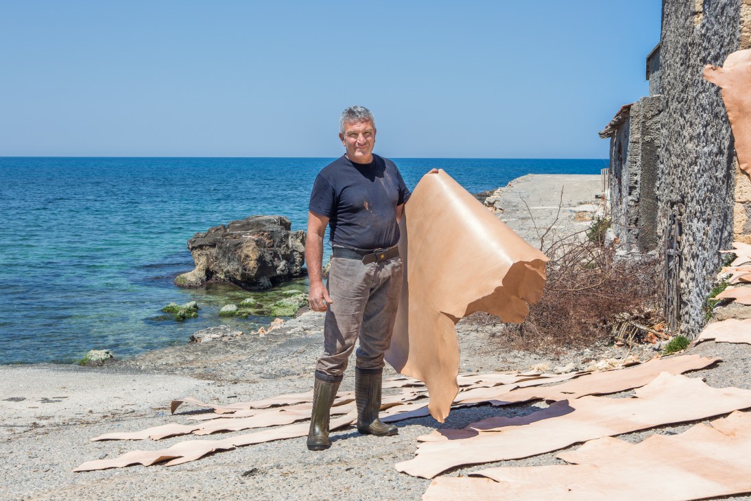 Man holding a large piece of leather by the sea at a tannery in Chania, Crete.