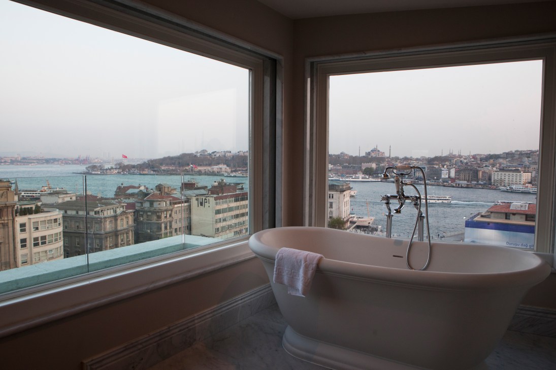 Modern freestanding bathtub with views of Istanbul's waterfront and cityscape through floor-to-ceiling windows.