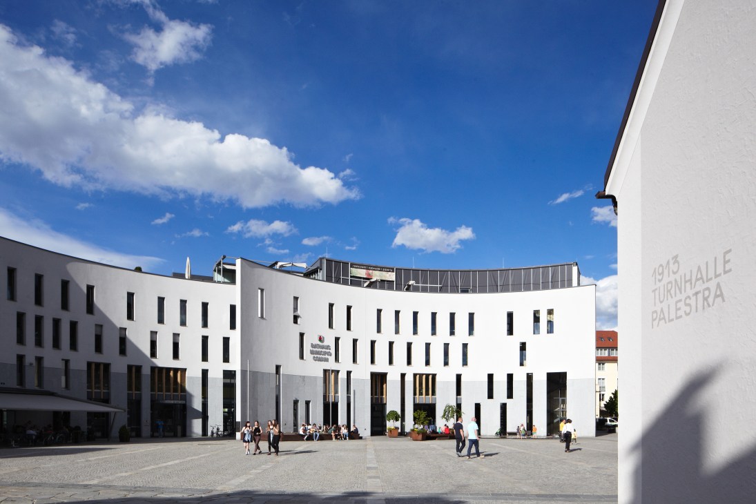 Modern white city hall building with regular window pattern facing a plaza in Brunico, South Tyrol.