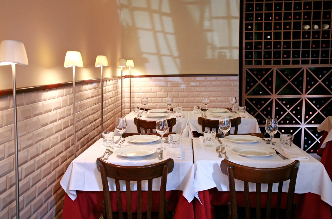 Elegant dining room with white tablecloths, wine storage, and modern lighting at Metodo Classico restaurant.