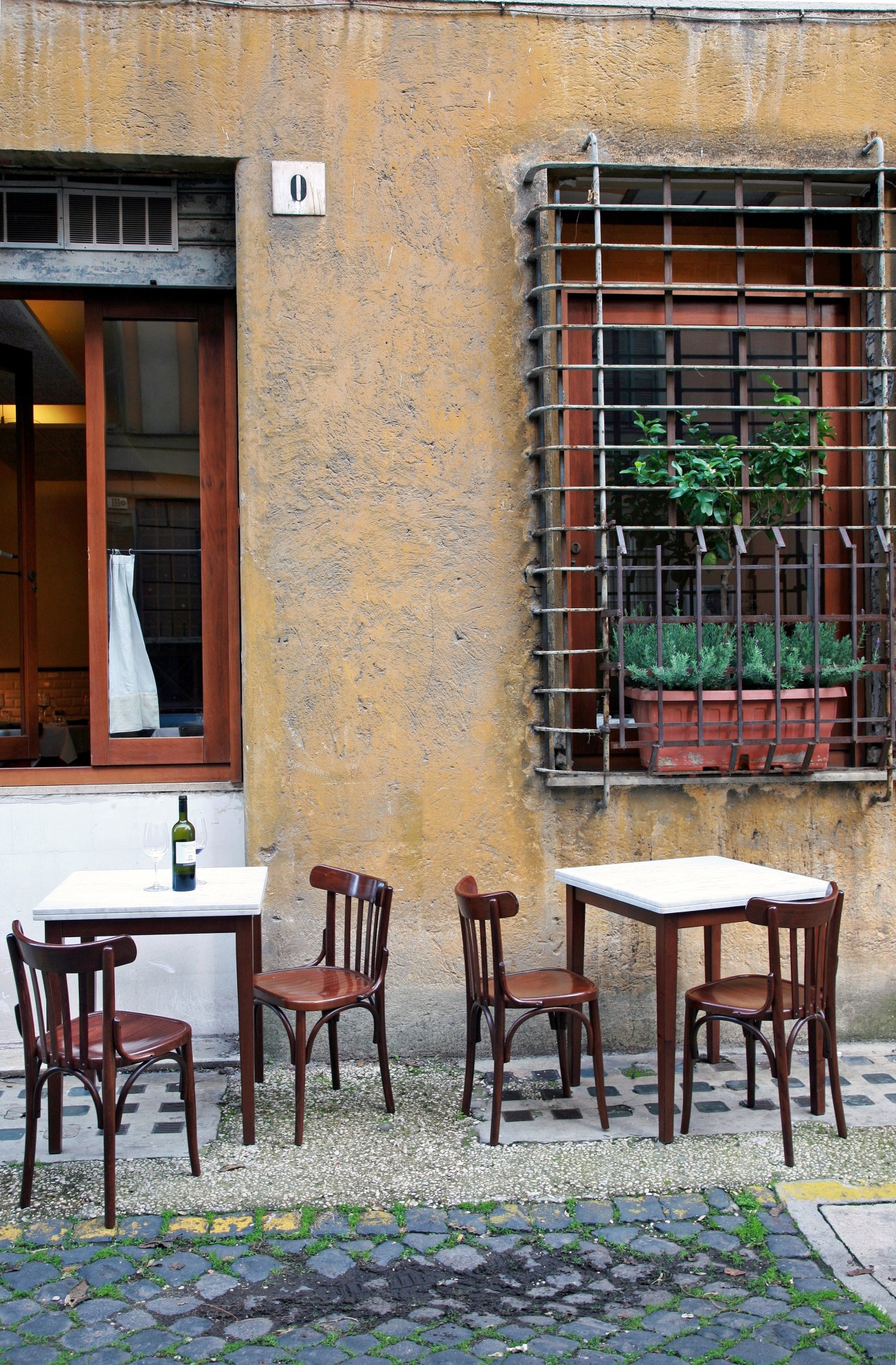 Metodo Classico restaurant's outdoor seating with wooden chairs and tables against a weathered yellow building facade in Rome.