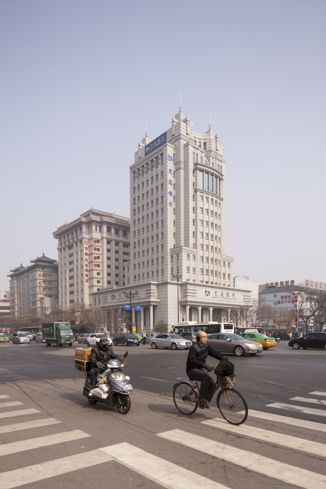 A busy crossroads in Xi'an's Hi-Tech Development Zone with modern high-rise buildings, vehicles, and pedestrians on bicycles.