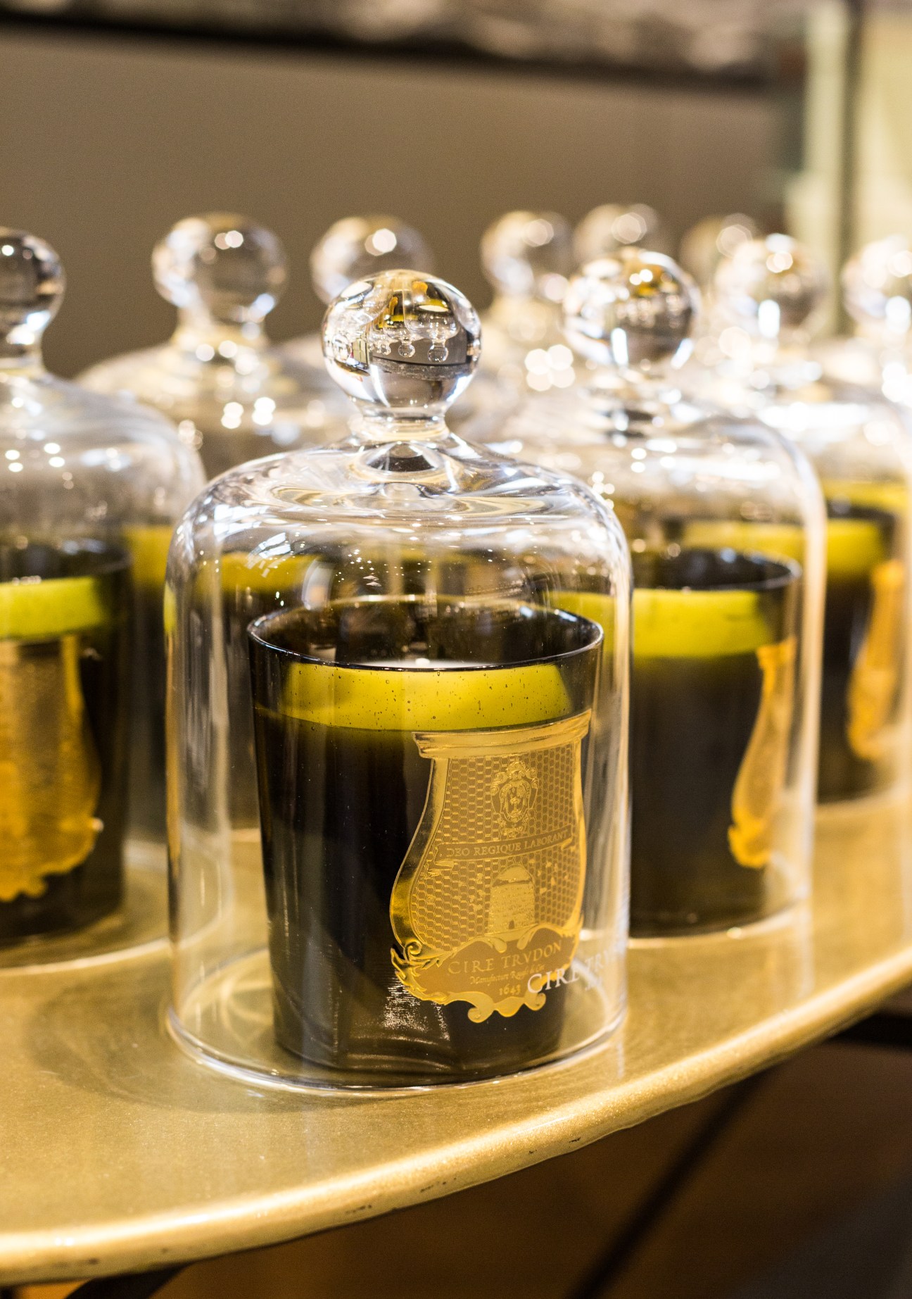 Glass jars with spherical lids containing dark liquid and yellow-labeled bottles arranged on a wooden tray.