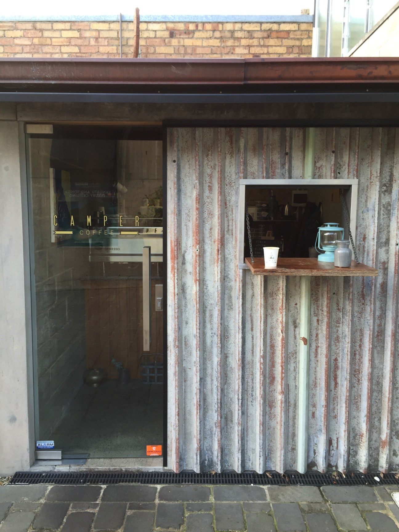 Camper coffee shop storefront in Auckland with weathered corrugated metal siding and service window displaying espresso equipment.