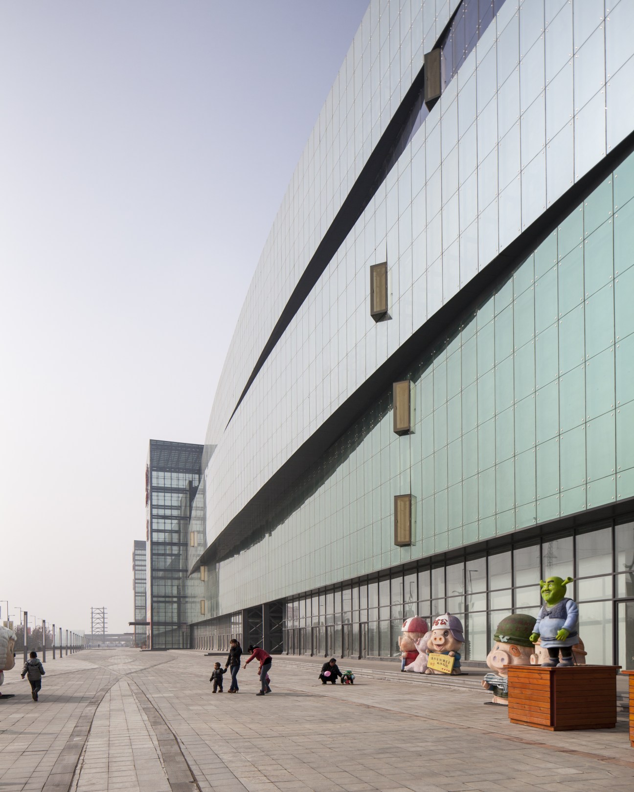 Modern glass-fronted building with geometric design and cartoon character statues on a paved plaza.