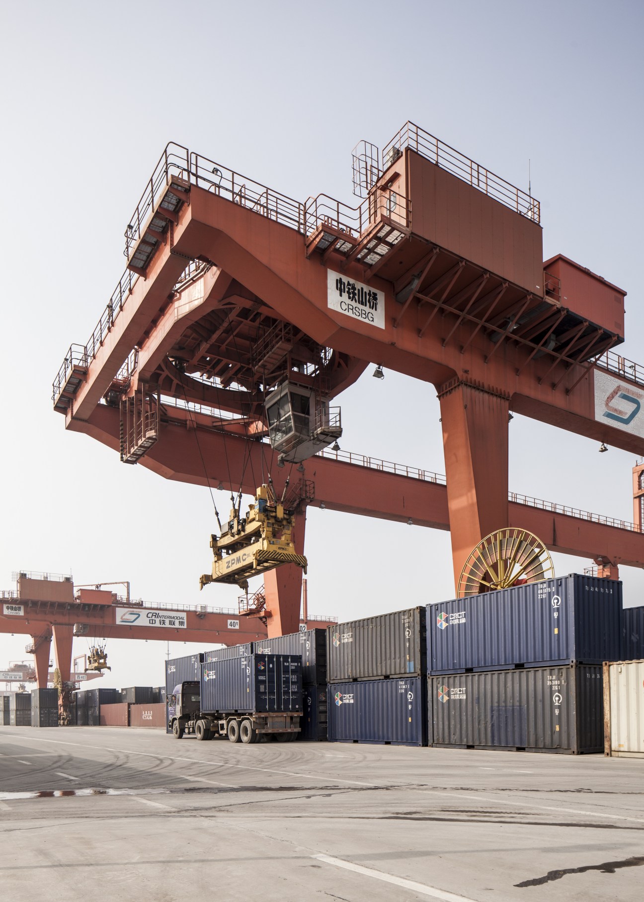 Large red industrial gantry crane lifting shipping containers at Xi'an's International Trade and Logistics Park.
