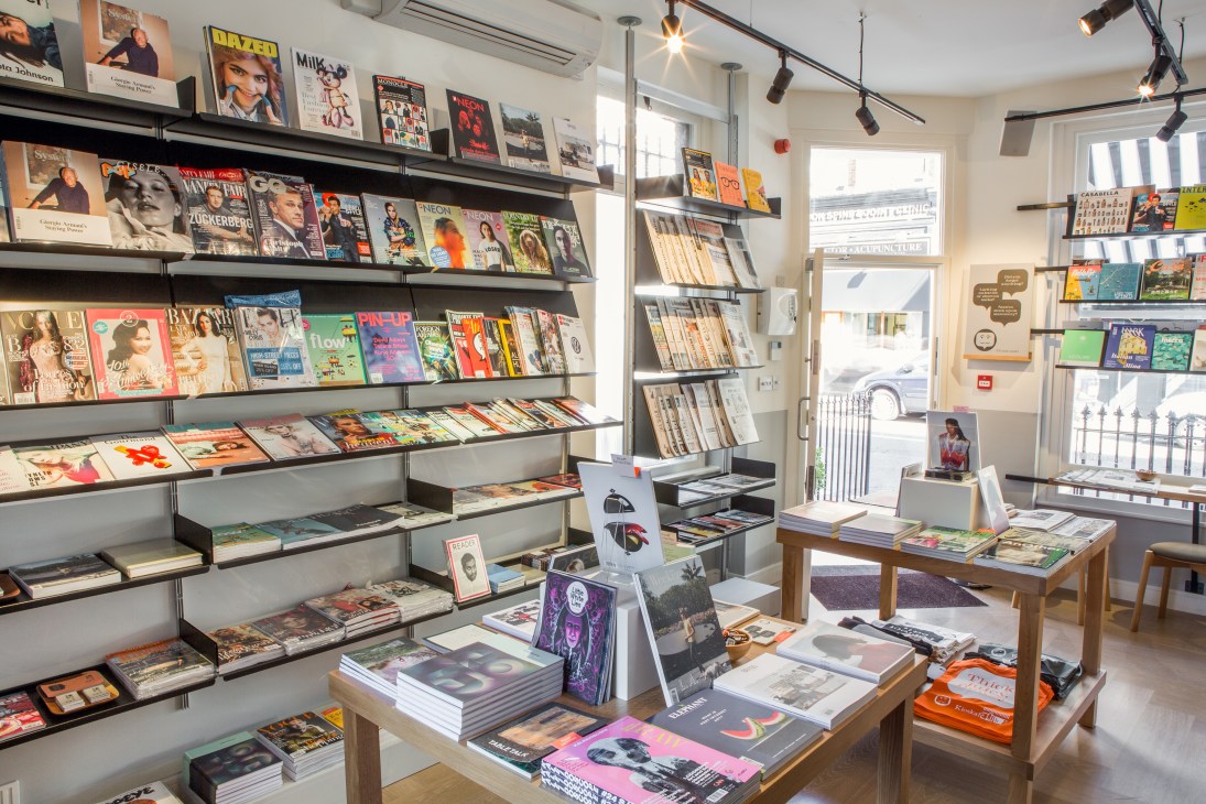 Interior of Kioskafé newsstand displaying magazines, books, and publications on wall-mounted shelves