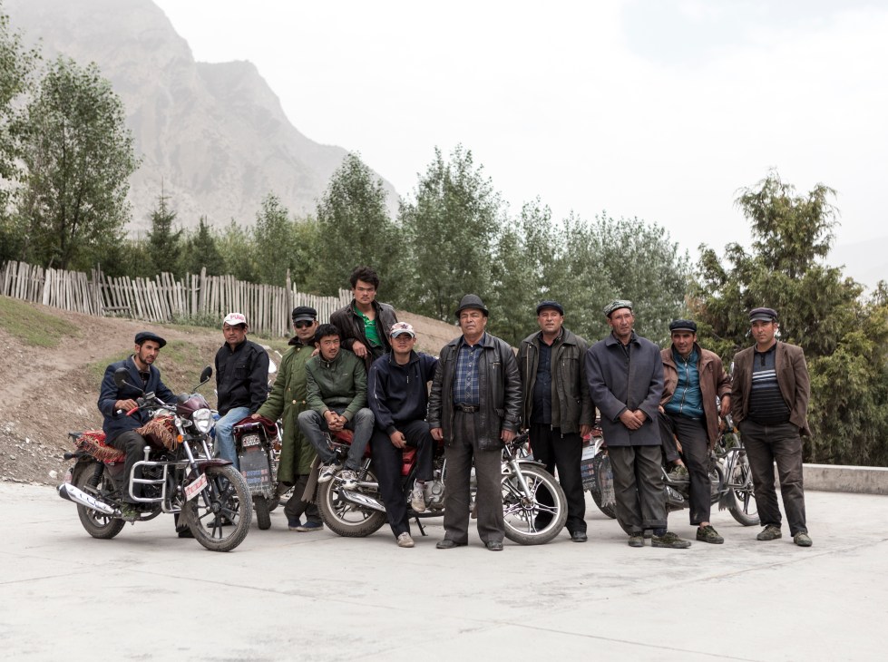 Group of Kyrgyz men posing with motorcycles and bicycles against mountain backdrop in Akto County.