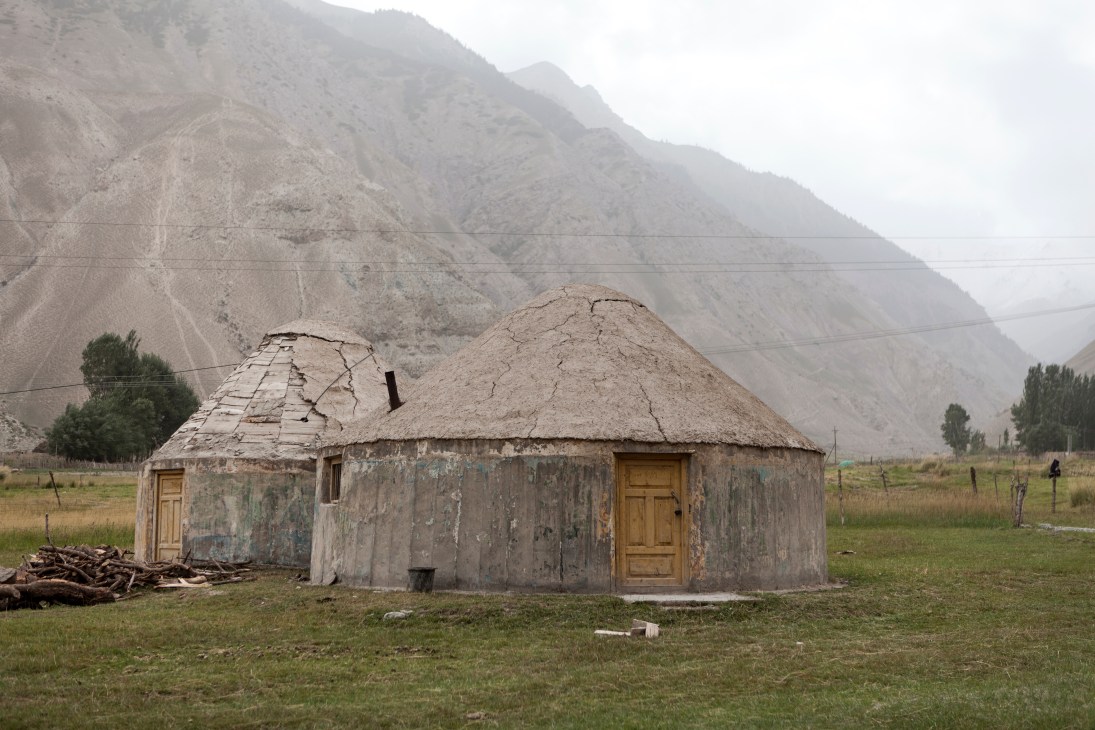 Weathered yurt hotel with thatched roof in mountain valley landscape at Kizilsu Glacier Park.